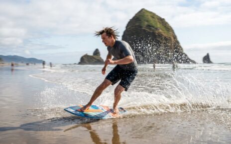 A high-end skimboard resting on the wet sand of a misty Oregon beach.