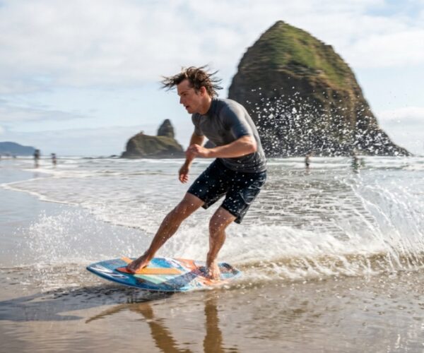 A high-end skimboard resting on the wet sand of a misty Oregon beach.